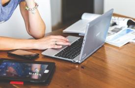 A lady sat at a desk working remotely with laptop, tablet and mobile phone