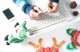 A person holding a credit card on a laptop keyboard with Christmas decorations surrounding it. 